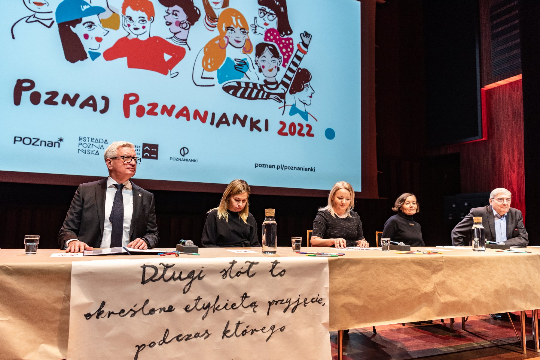 Na zdjęciu pięć osób za stołem, wśród nich prezydent Poznania, w tle ekran z rysunkiem kobiet i napisem: poznaj poznanianki 2022 - grafika artykułu