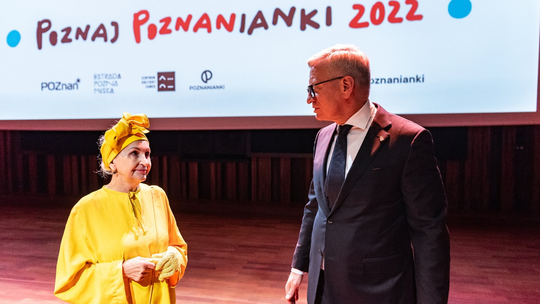 Na zdjęciu Jacek Jaśkowiak i ubrana na żółto seniorka, rozmawiają. W tle napis: poznaj Poznanianki 2022
