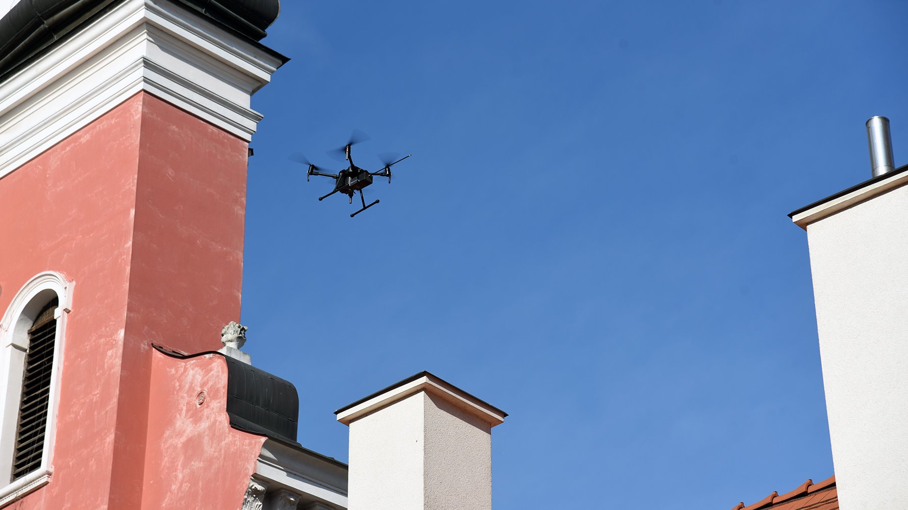 Na zdjęciu dron latający między budynkami