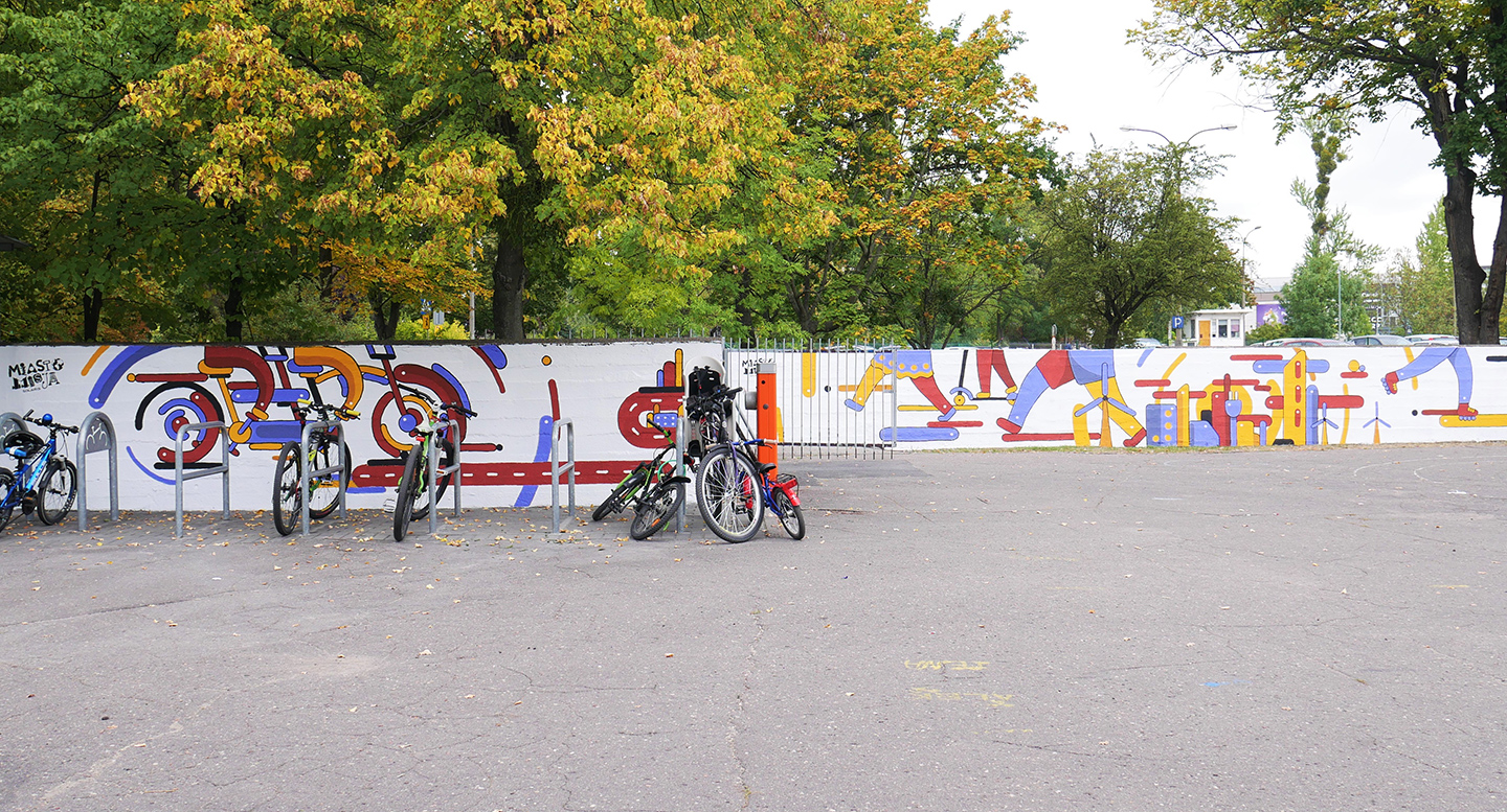 Zdjęcie przedstawia mural wykonany na ogrodzeniu szkoły, przed nim stoją rowery - grafika artykułu