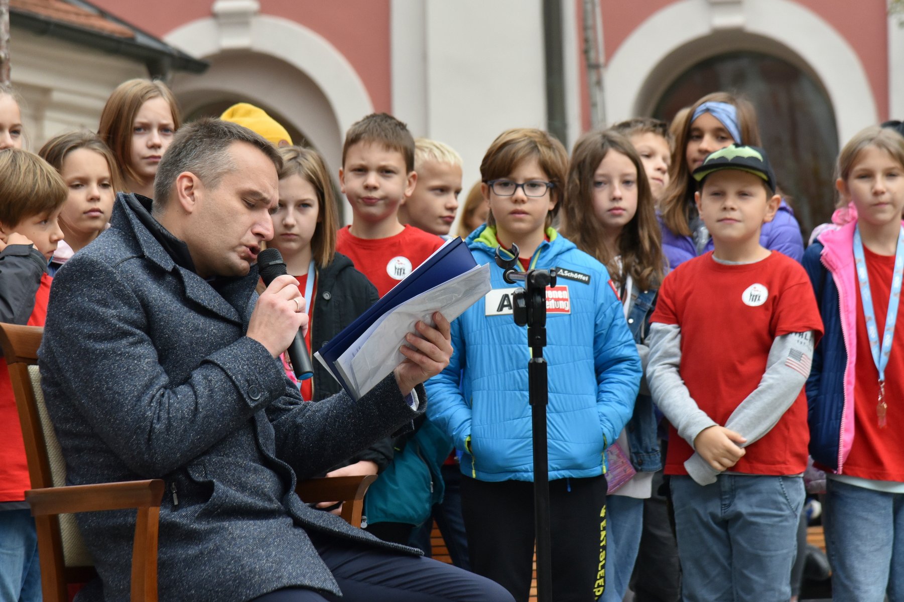 Na zdjęciu Mariusz Wiśniewski, zastępca prezydenta Poznania, czytający tekst, za nim dzieci - grafika artykułu