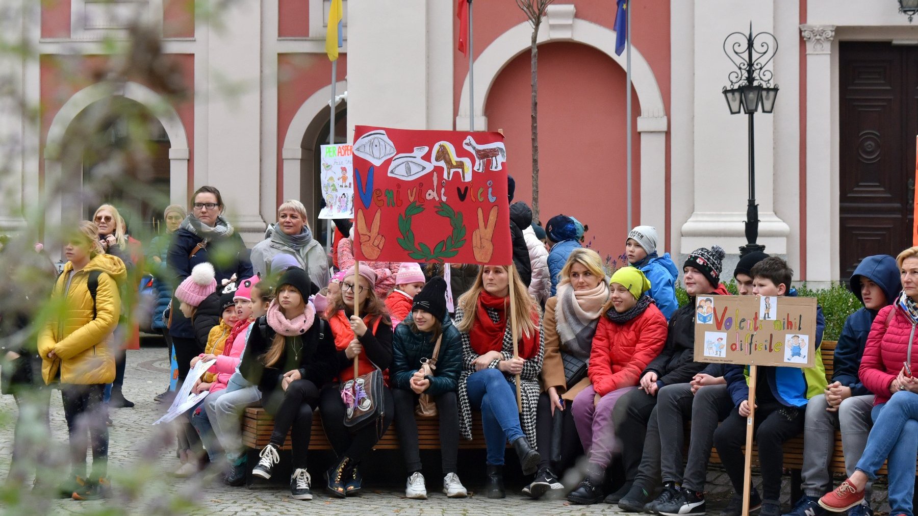 Na zdjęciu dzieci na dziedzińcu urzędu, trzymające transparenty