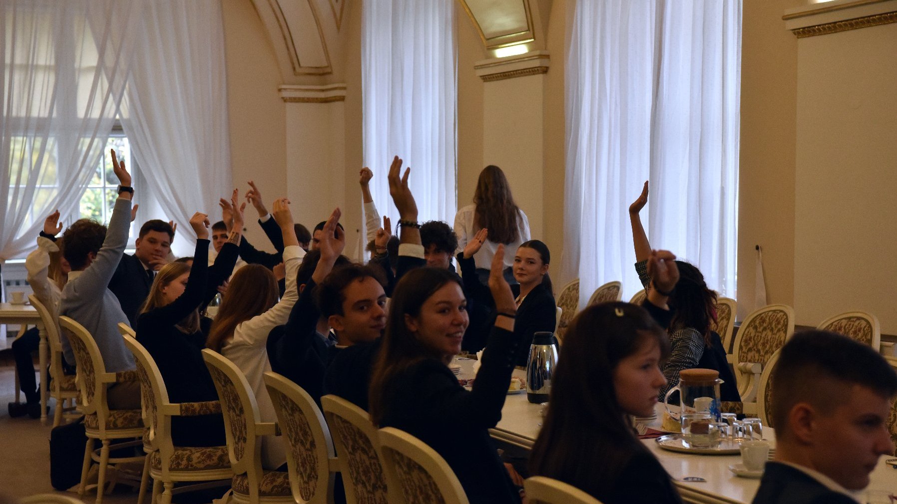 Na zdjęciu członkowie młodzieżowej rady miasta siedzący w sali z podniesionymi rękoma