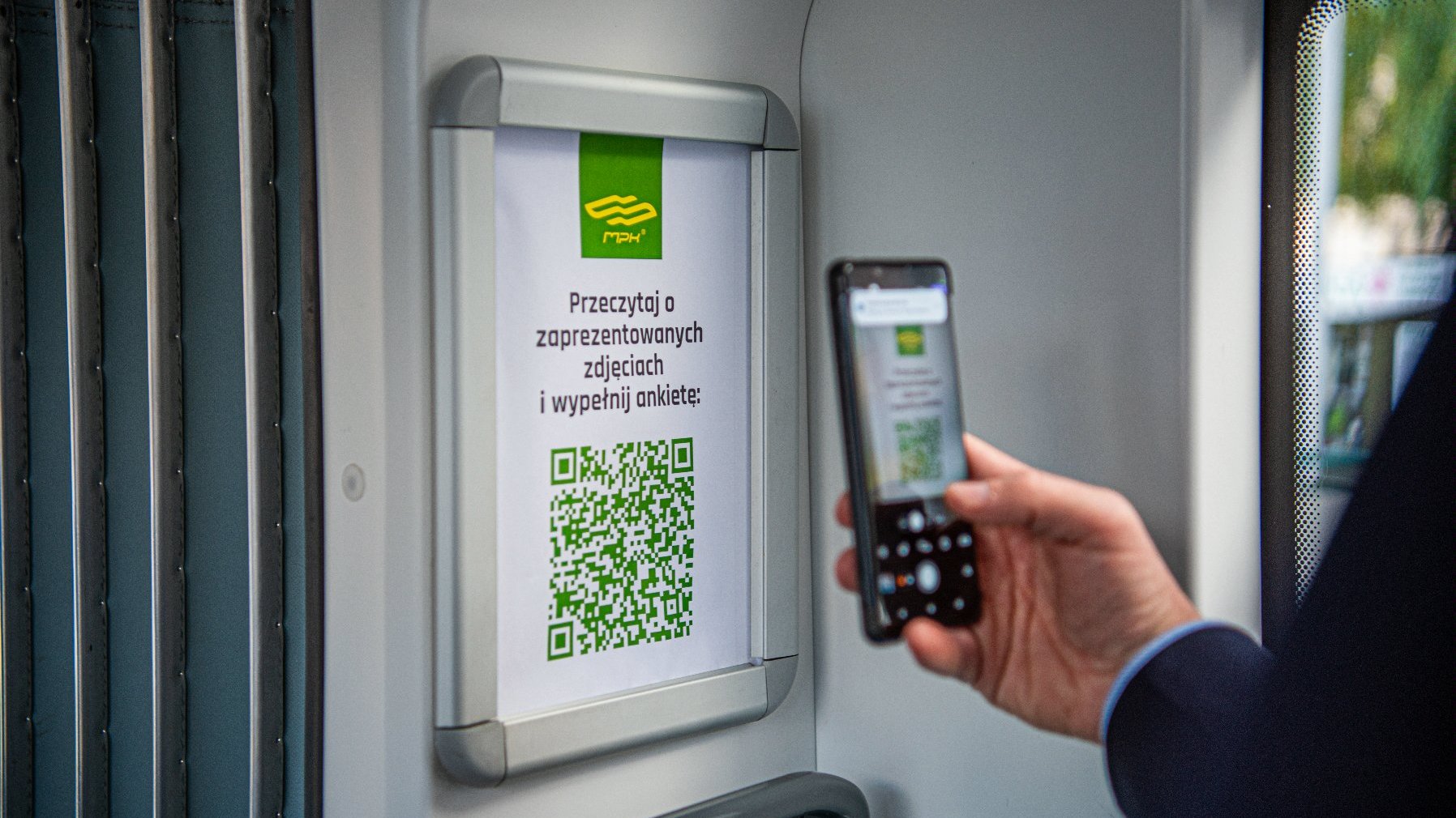 Na zdjęciu dłoń z telefonem, ktoś robi zdjęcie kodu QR w tramwaju