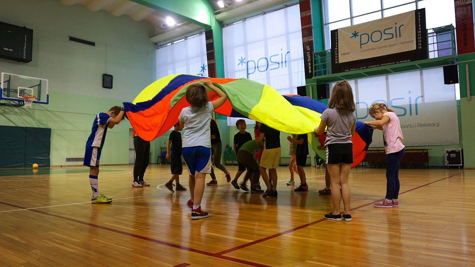 Akcja Zima z POSiR - Dzieci bawią się kolorową chustą na sali sportowej