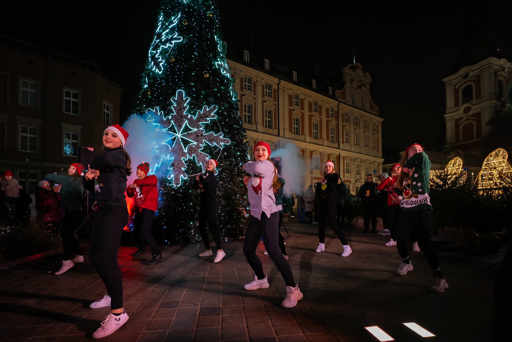 Zdjęcie przedstawia grupę tancerzy w czapkach św. Mikołaja. W tle choinka. - grafika artykułu