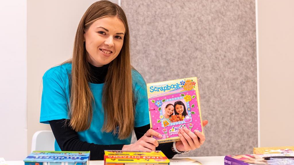 Na zdjęciu uśmiechnięta dziewczyna pokazująca zabawkę dla dzieci