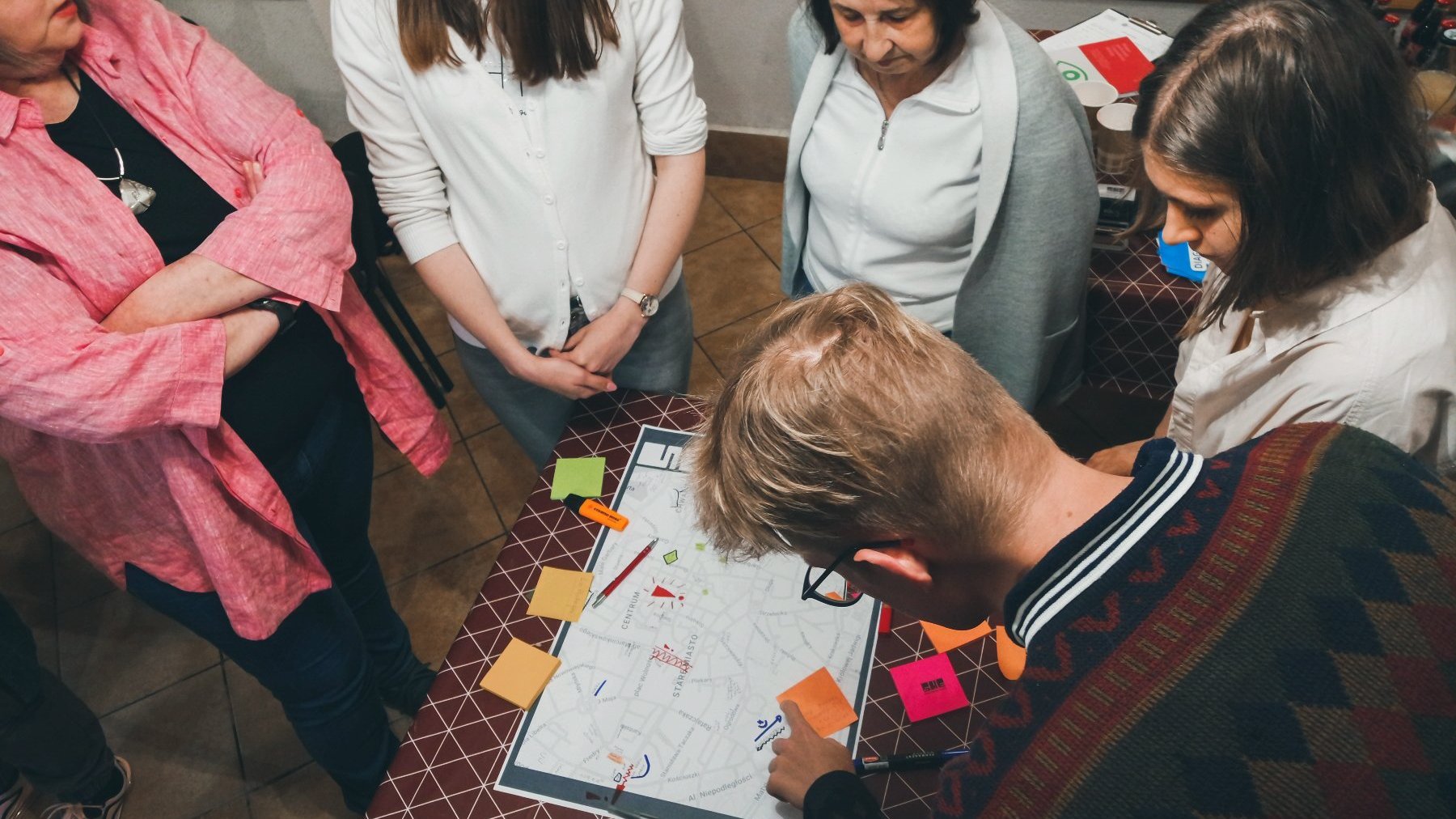 Na zdjęciu grupa ludzi pochylonych nad stołem, na stole schematyczna mapa