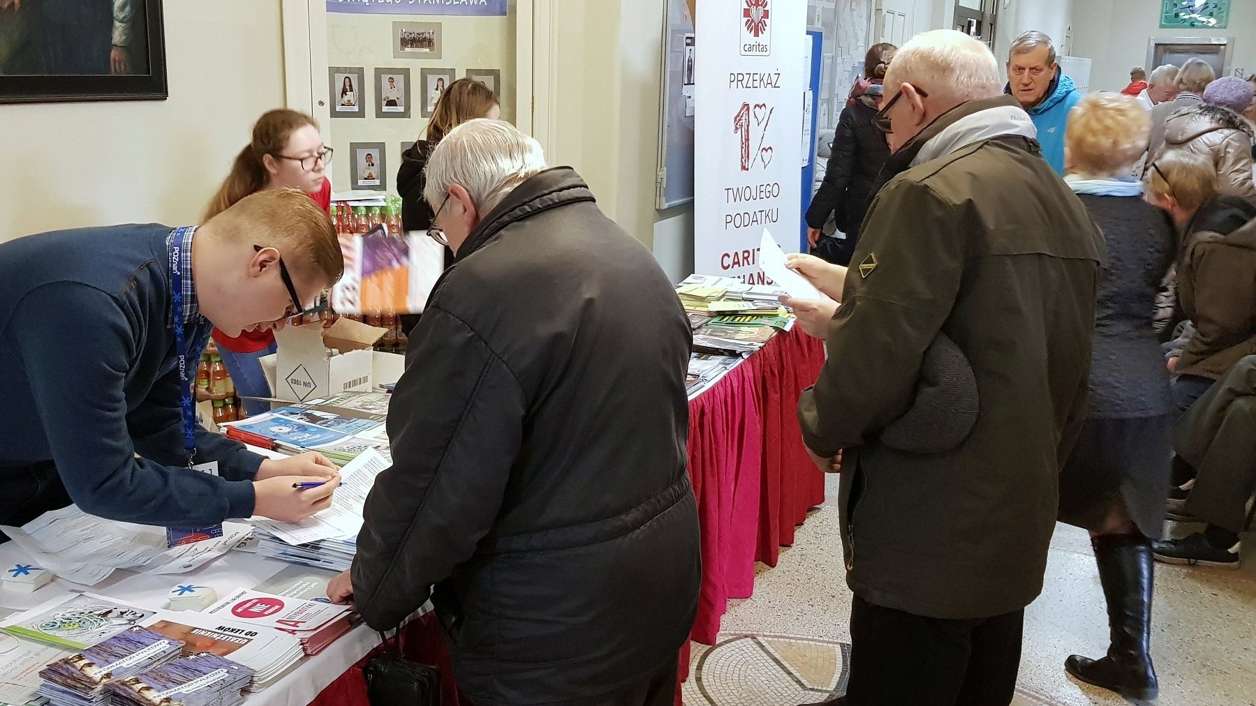 Na zdjęciu ludzie w szkolnym korytarzu, widać stoiska