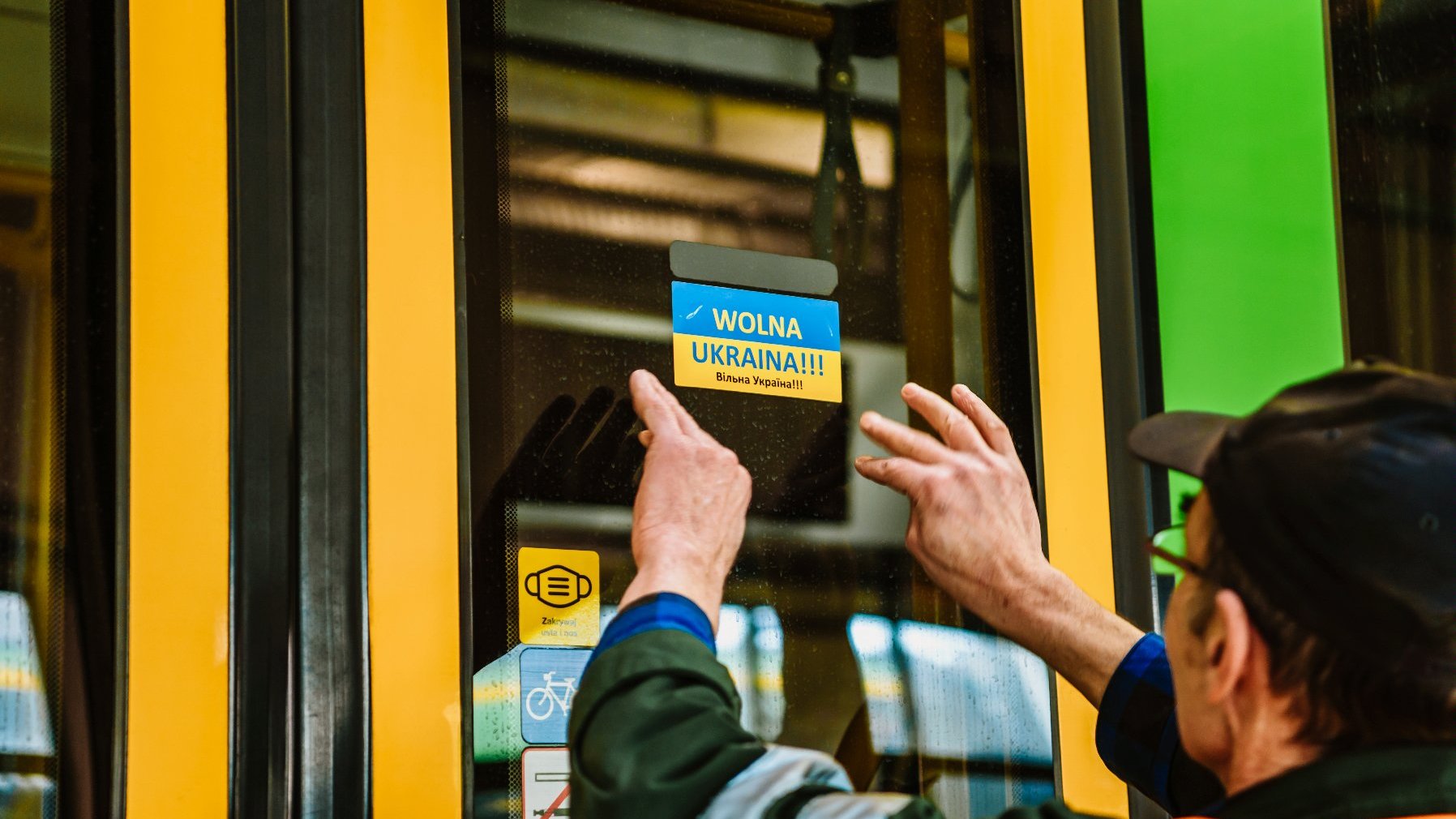 Na zdjęciu pracownik MZK przyklejający na drzwiach tramwaju naklejkę z napisem Wolna Ukraina