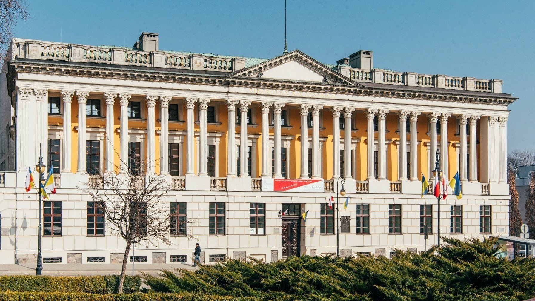 Zdjęcie przedstawia elewację frontową budynku Biblioteki Raczyńskich. Pierwsza kondygnacja wyłożona jest kamieniem, drugą zdobi kolumnada.