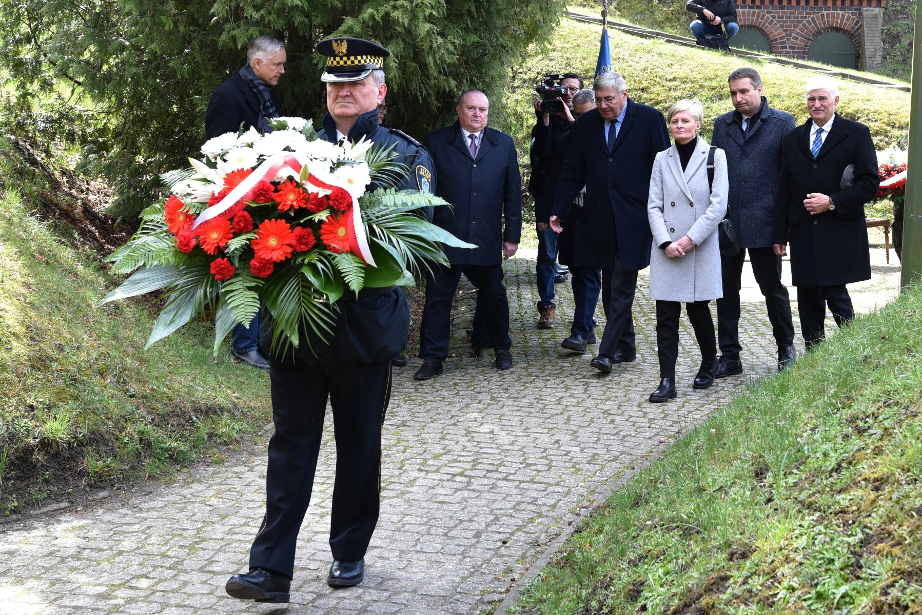 Na zdjęciu grupa osób składających wieniec z kwiatów - grafika artykułu