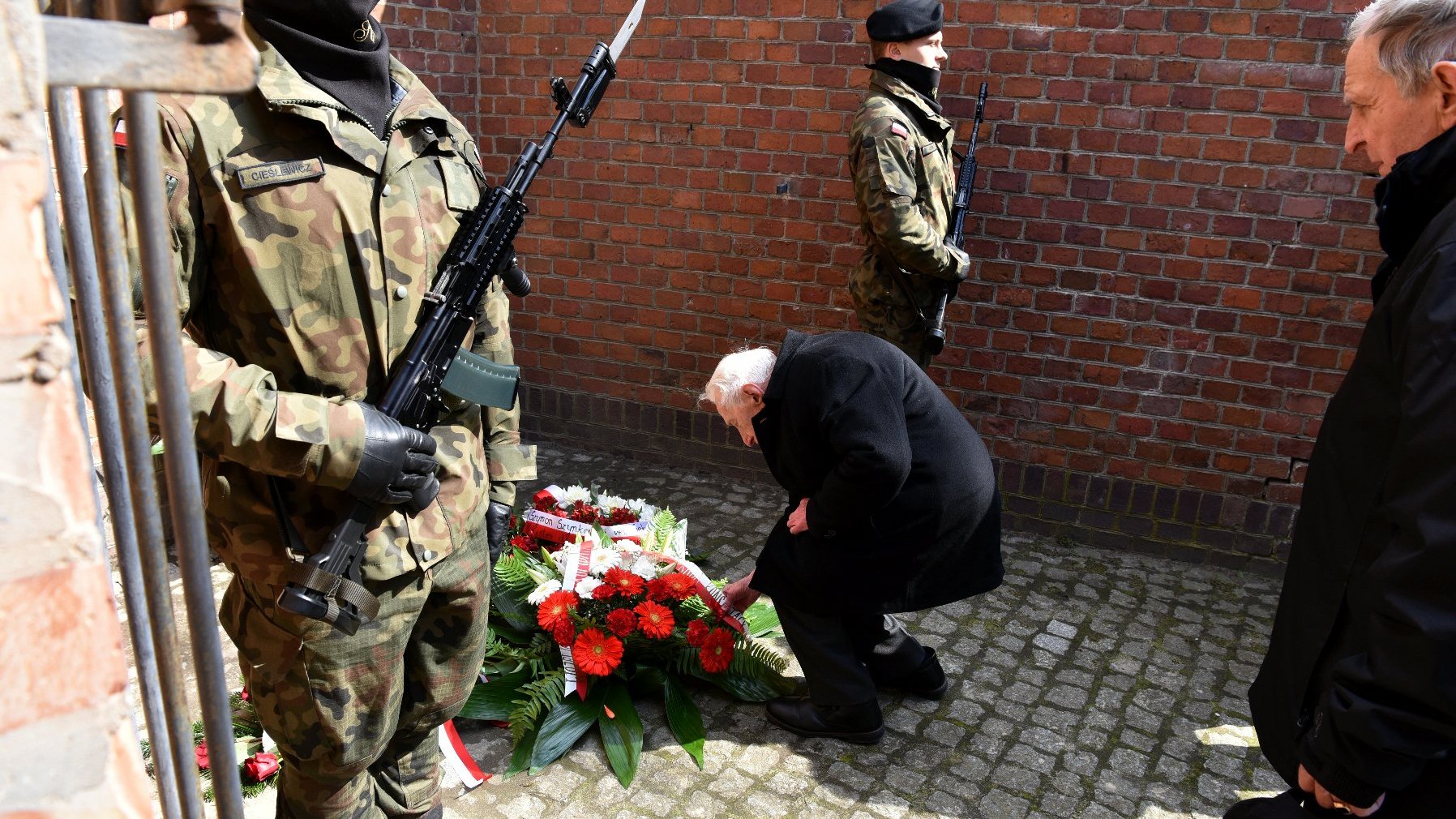 Na zdjęciu starszy mężczyzna składający kwiaty pod Ścianą Śmierci