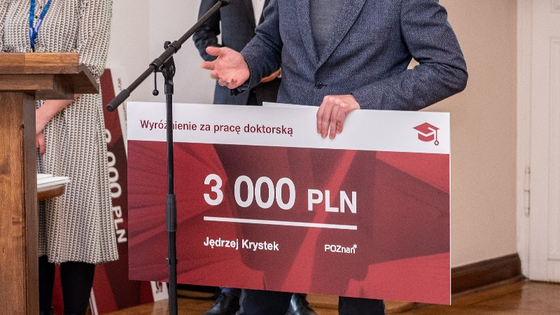 Na zdjęciu mężczyzna z czekiem przemawiający przed mikrofonem