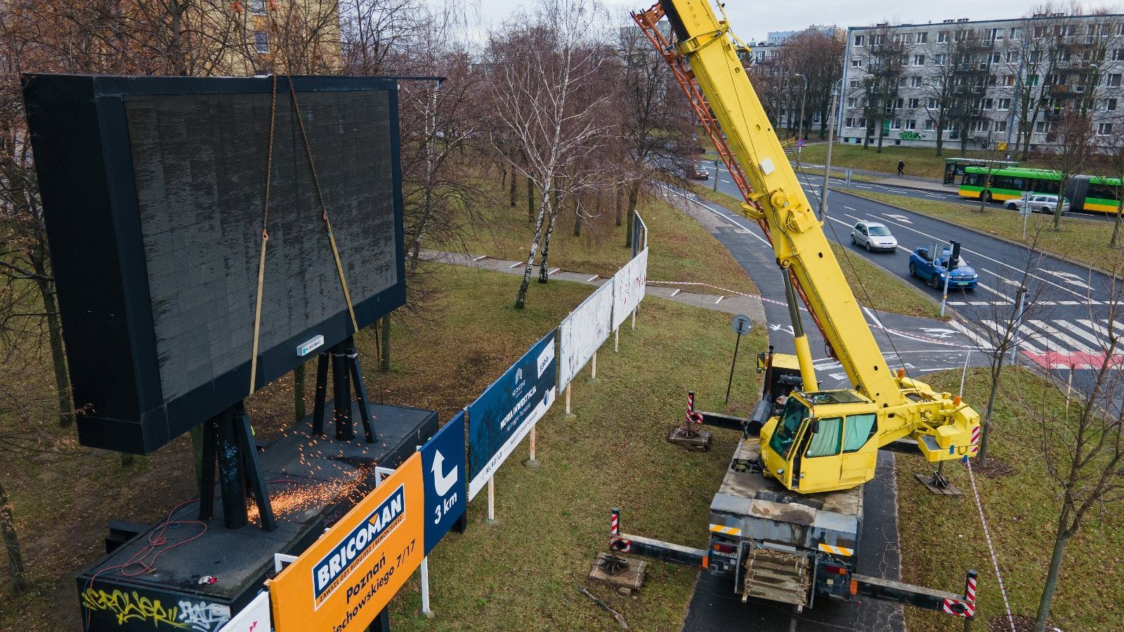 Zdjęcie przedstawia wielkoformatową tablicę LED demontowaną za pomocą dźwigu.