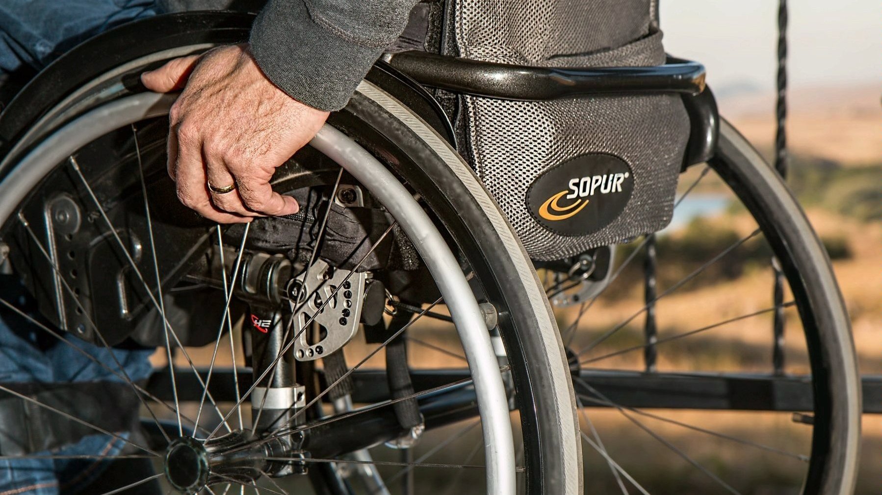 Na zdjęciu osoba na wózku, widać koła pojazdu i dłoń