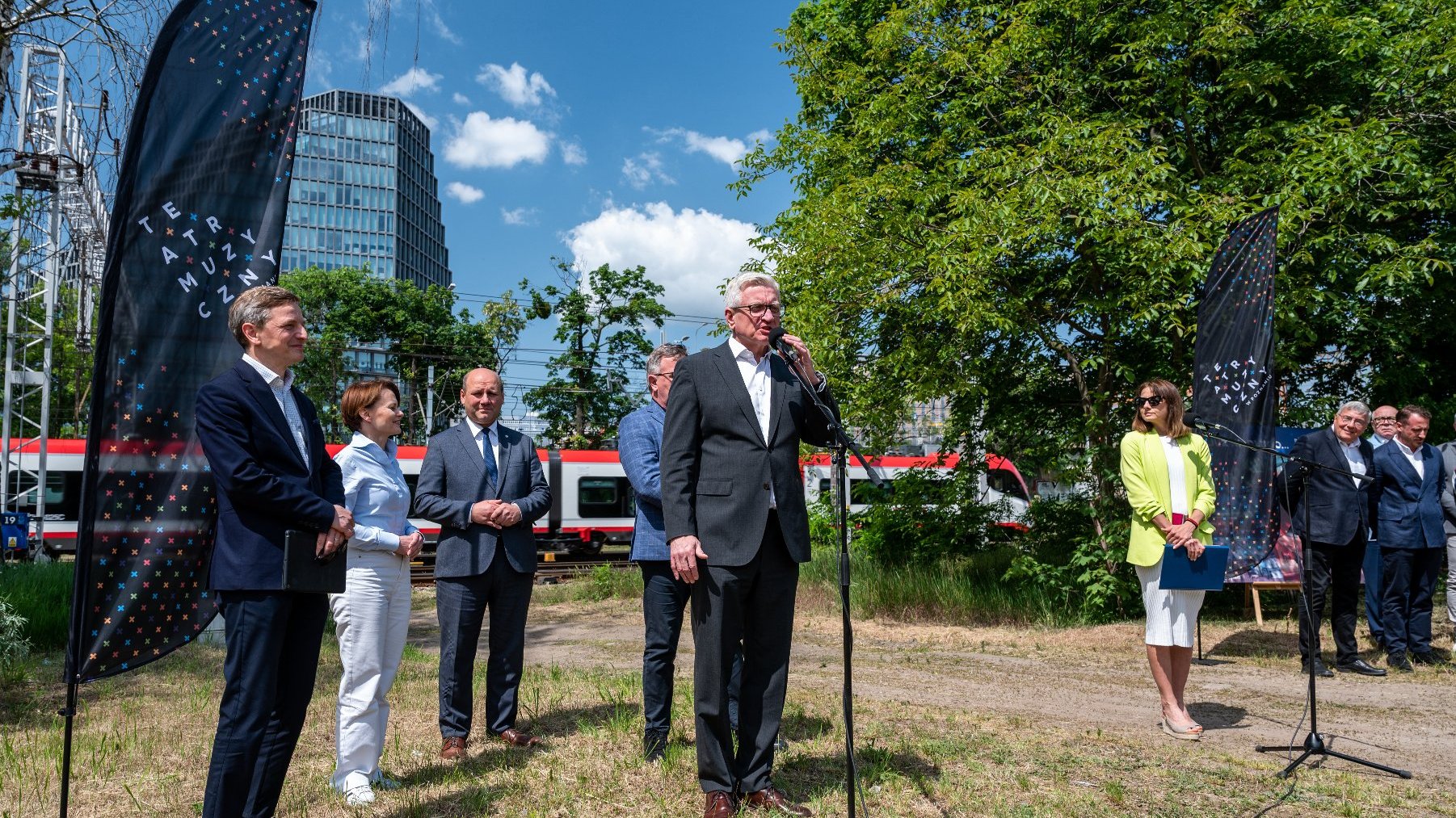 Zdjęcie przedstawia grupę osób podczas konferencji prasowej. W tle biurowiec "Bałtyk".