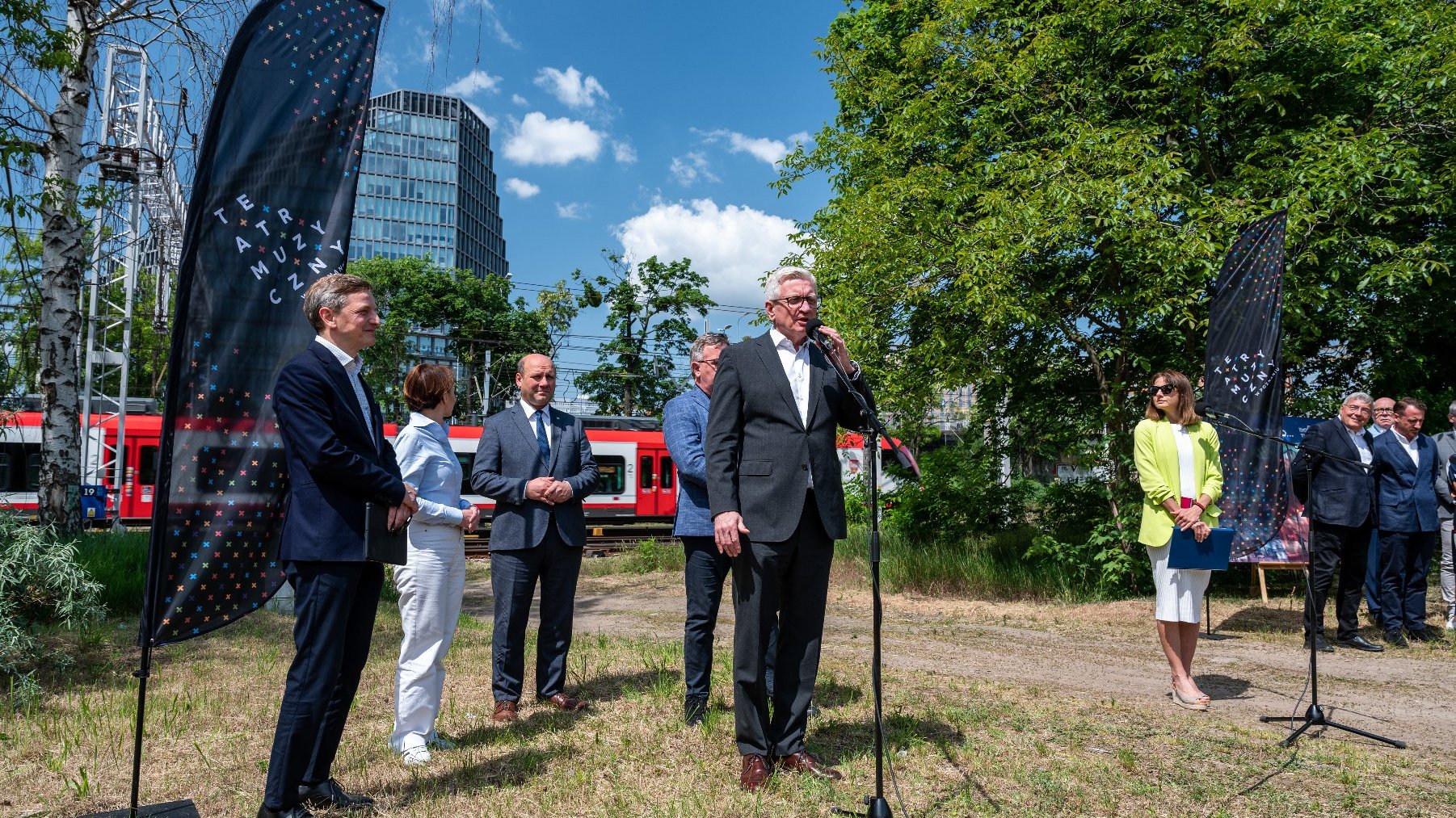 Zdjęcie przedstawia grupę osób podczas konferencji prasowej. W tle biurowiec "Bałtyk".