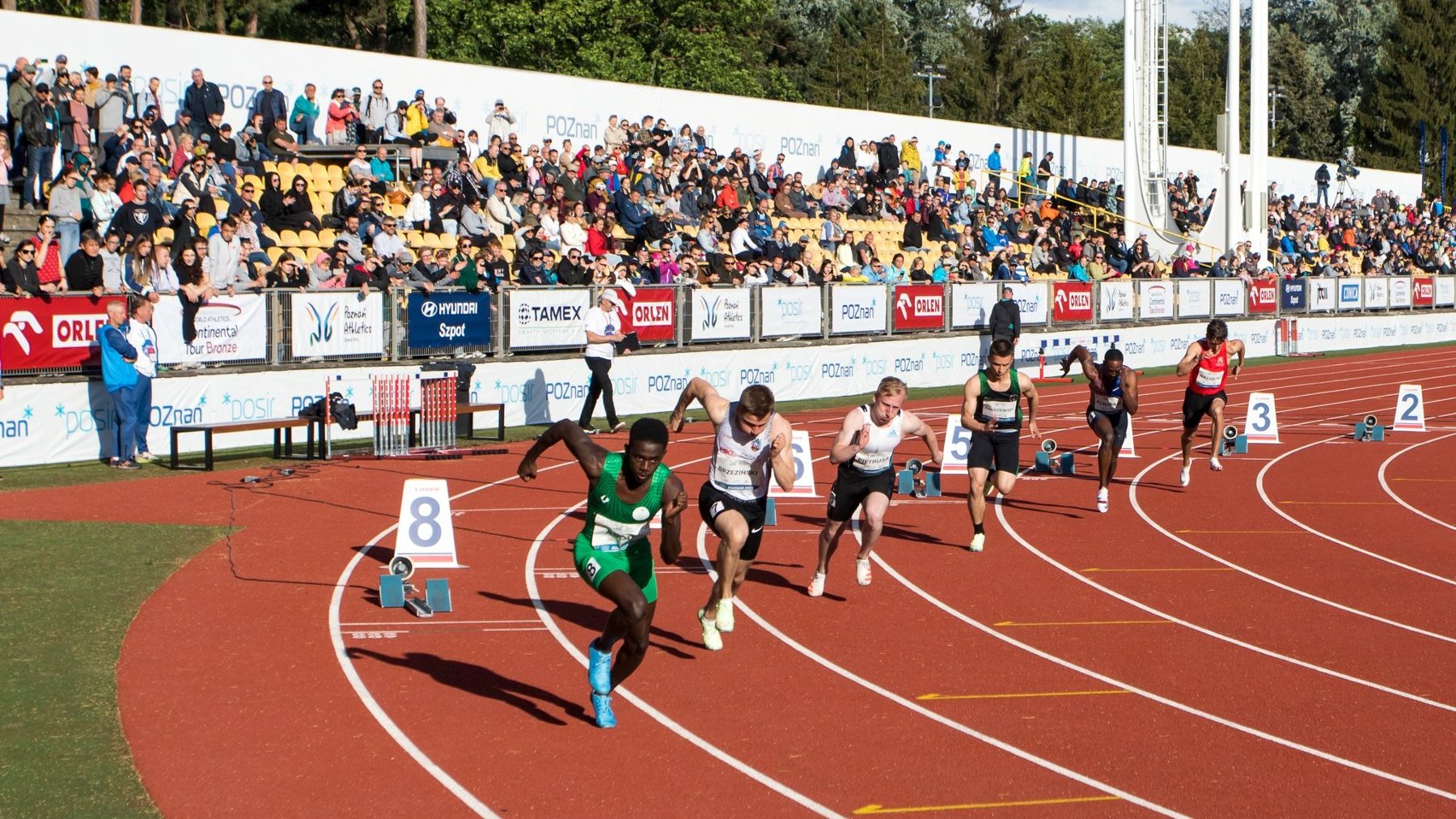 Start zawodników w biegu na 200 metrów. W tle publiczność na trybunach stadionu na Golęcinie