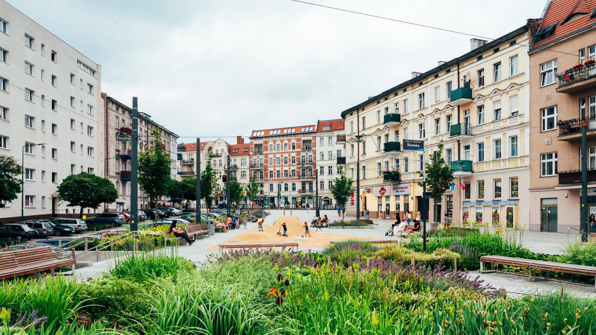 Na zdjęciu rynek Łazarski, na pierwszym planie rośliny, w tle bawiące się dzieci - grafika artykułu