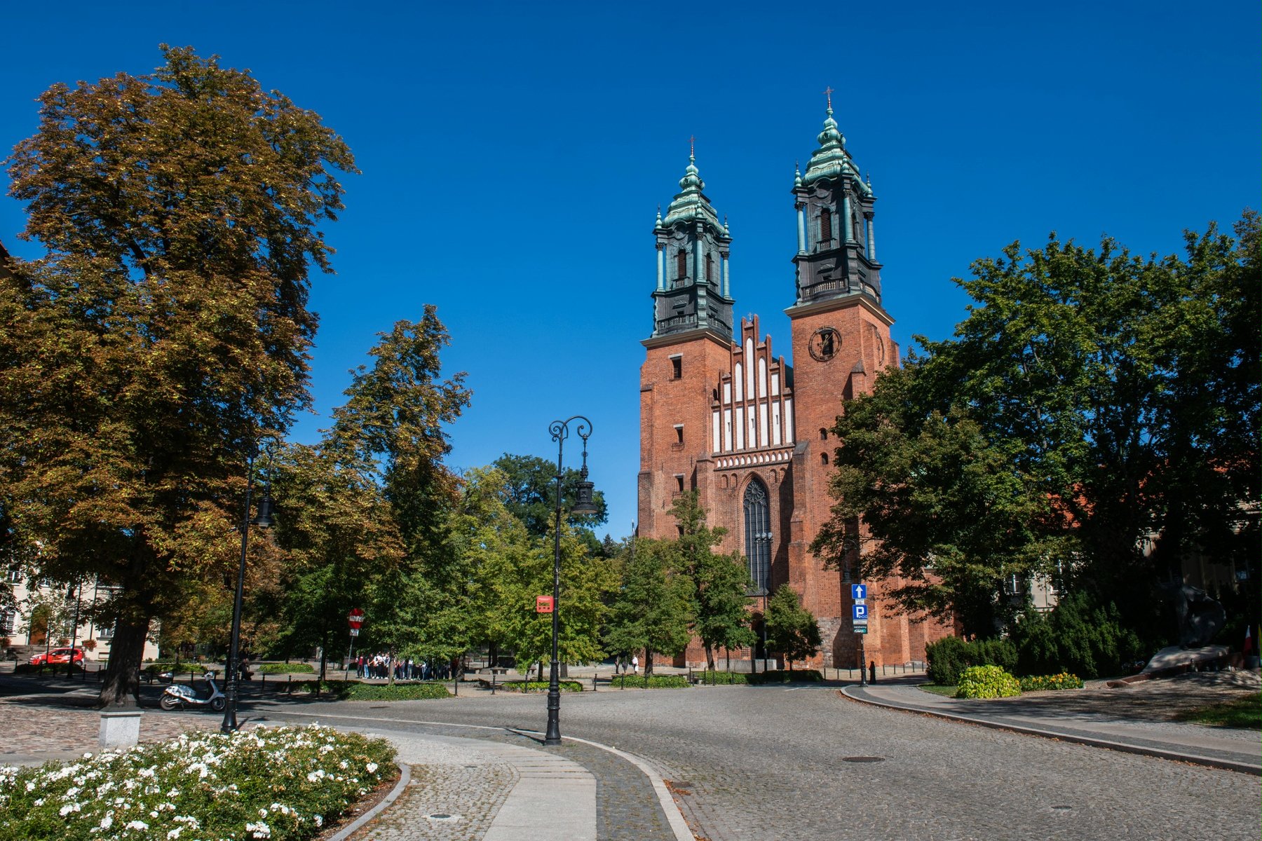 Zdjęcie przedstawia widok na katedrę poznańską, drogę oraz zieleń. - grafika artykułu