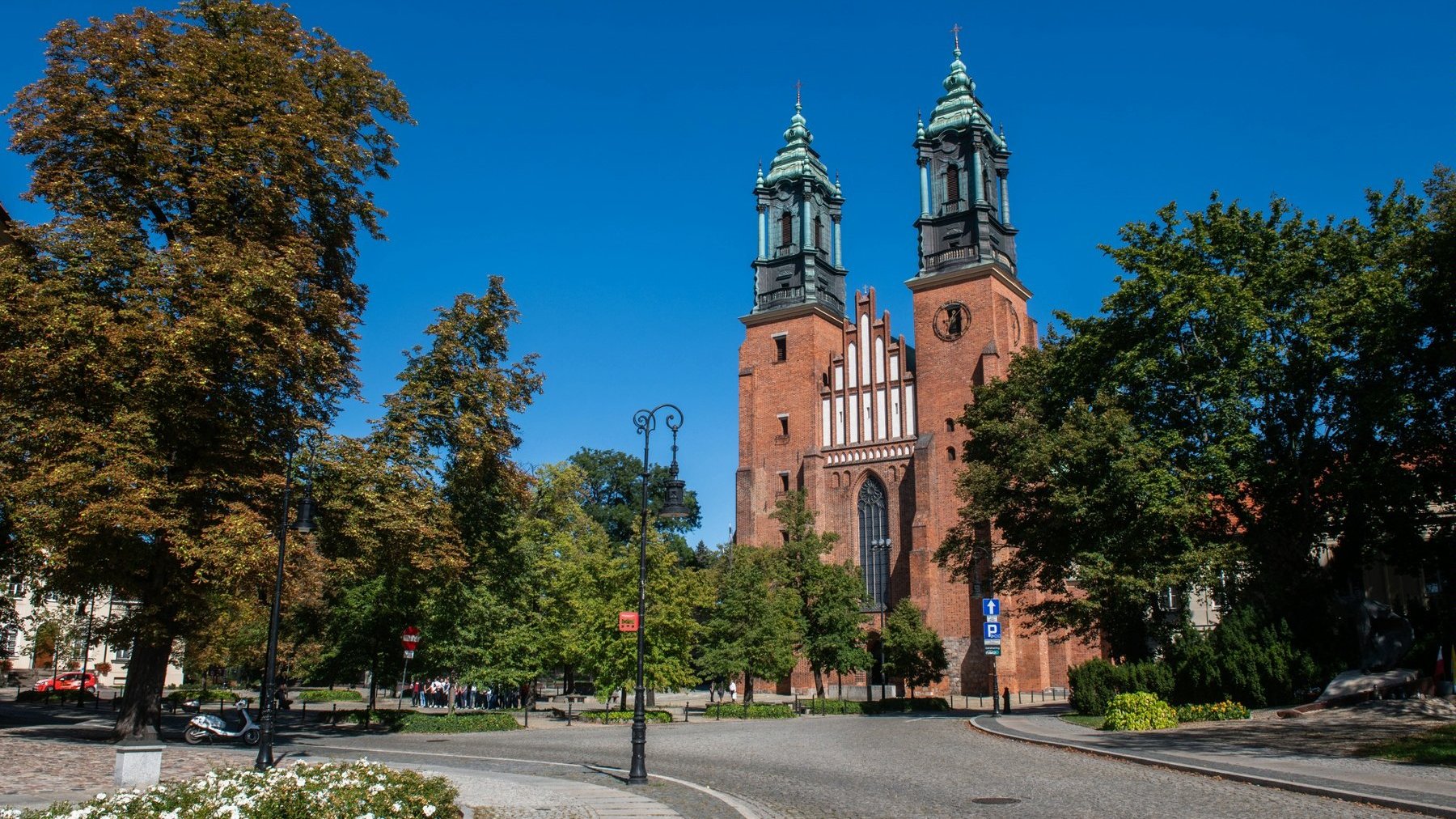 Zdjęcie przedstawia widok na katedrę poznańską, drogę oraz zieleń.