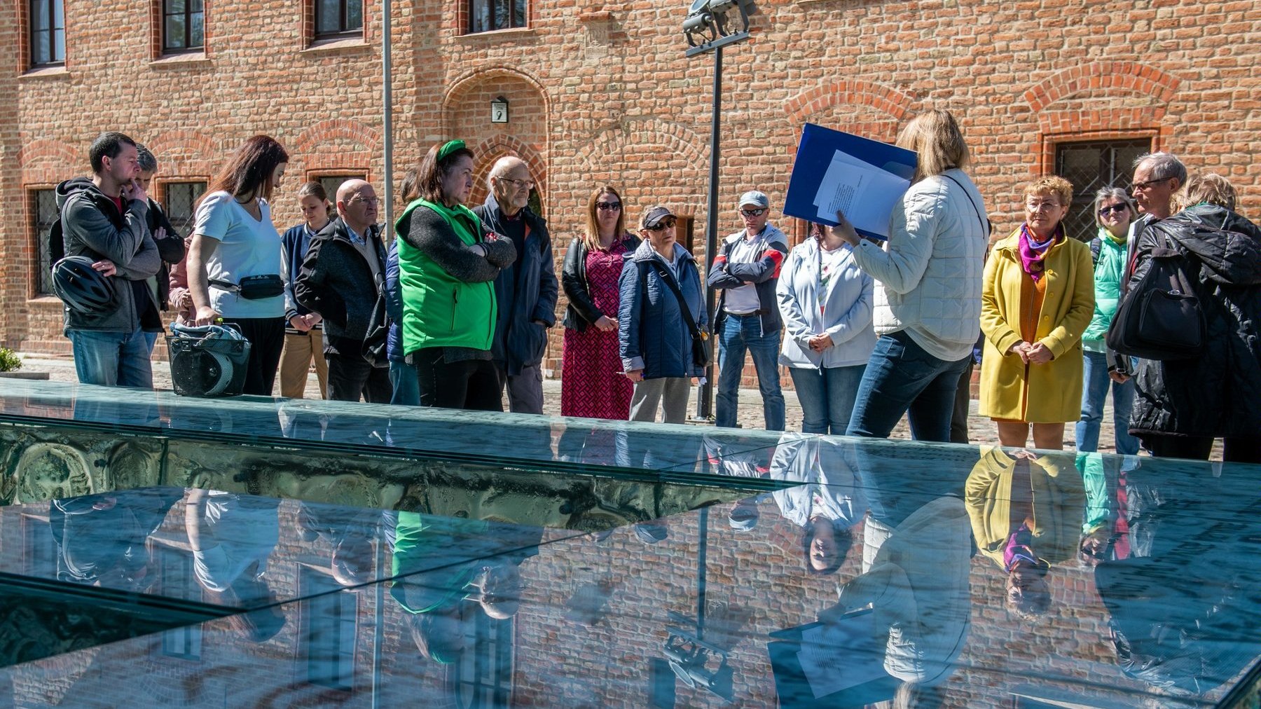 Zdjęcie przedstawia grupę ludzi podczas spaceru po Ostrowie Tumskim. Na pierwszym planie instalacja artystyczna wykonana ze szkła.