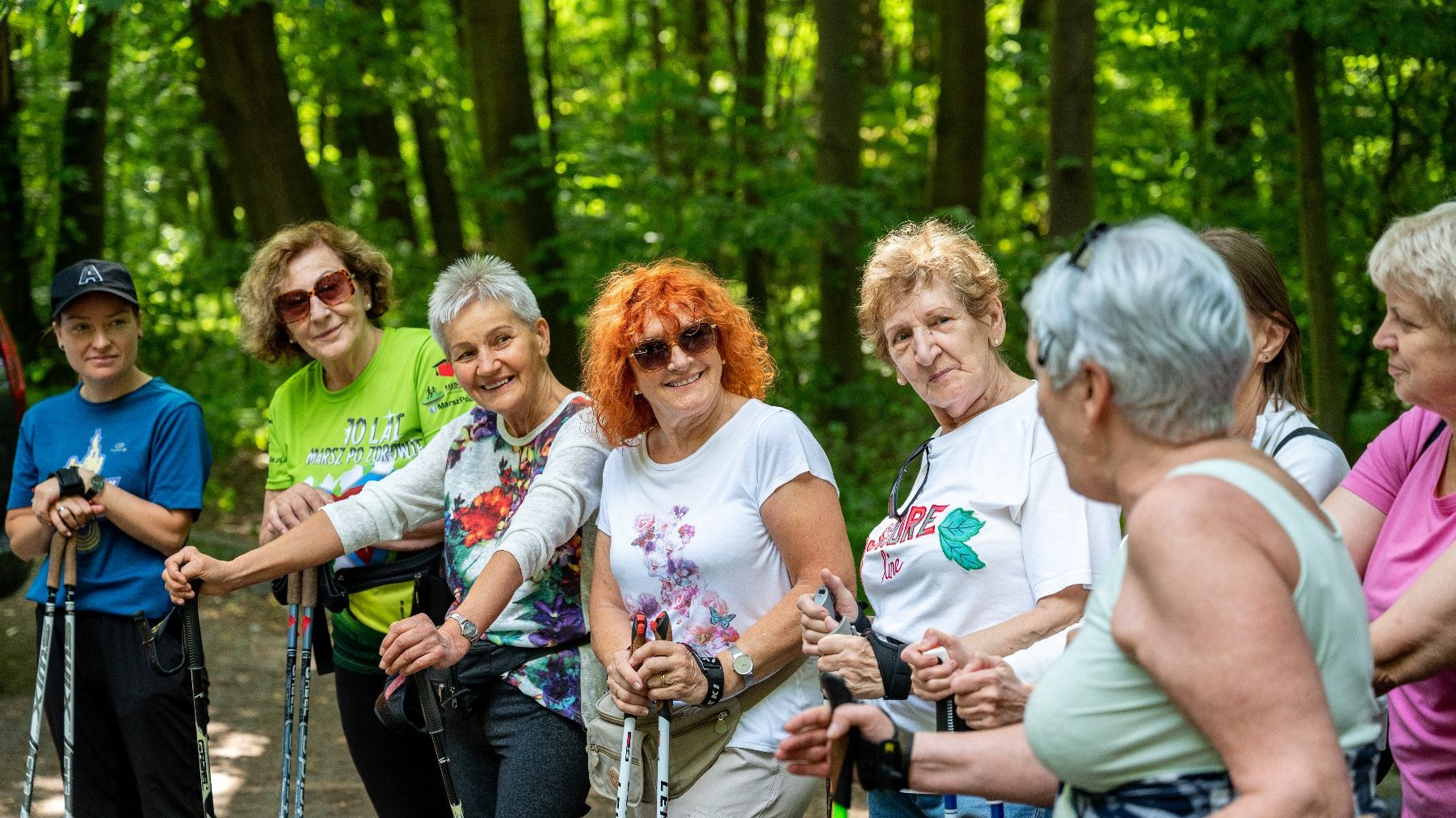 Galeria zdjęć przedstawia grupę seniorów w strojach sportowych z kijkami do nordic walking.