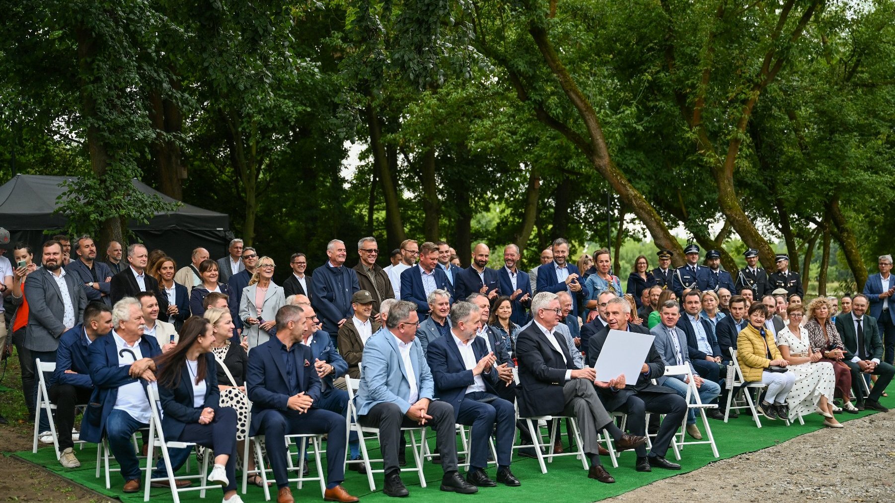 Na zdjęciu ludzie zgromadzeni przed kładką, część z nich siedzi na krzesłach