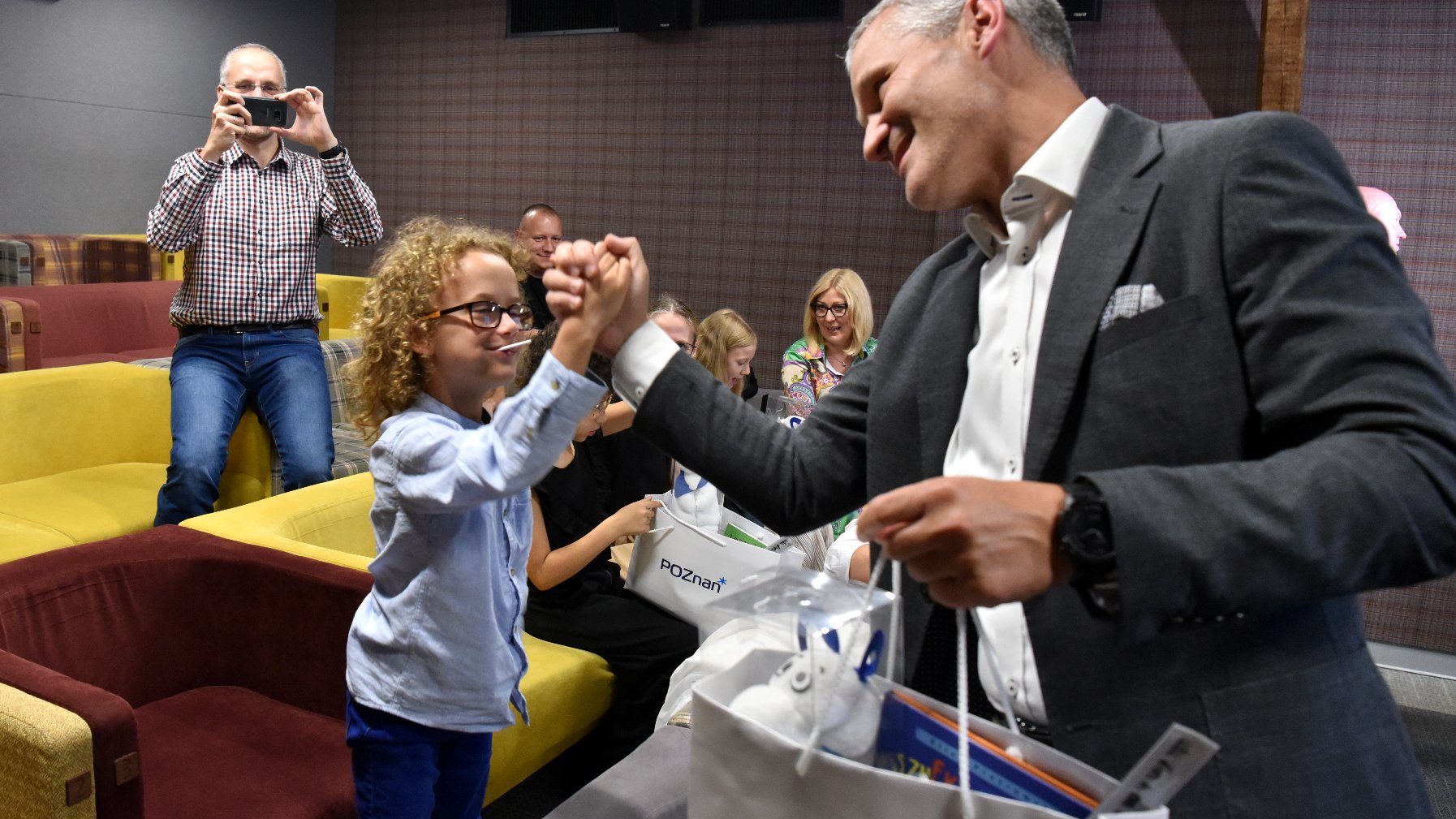 Na zdjęciu mężczyzna w garniturze przybijający piątkę dziecku