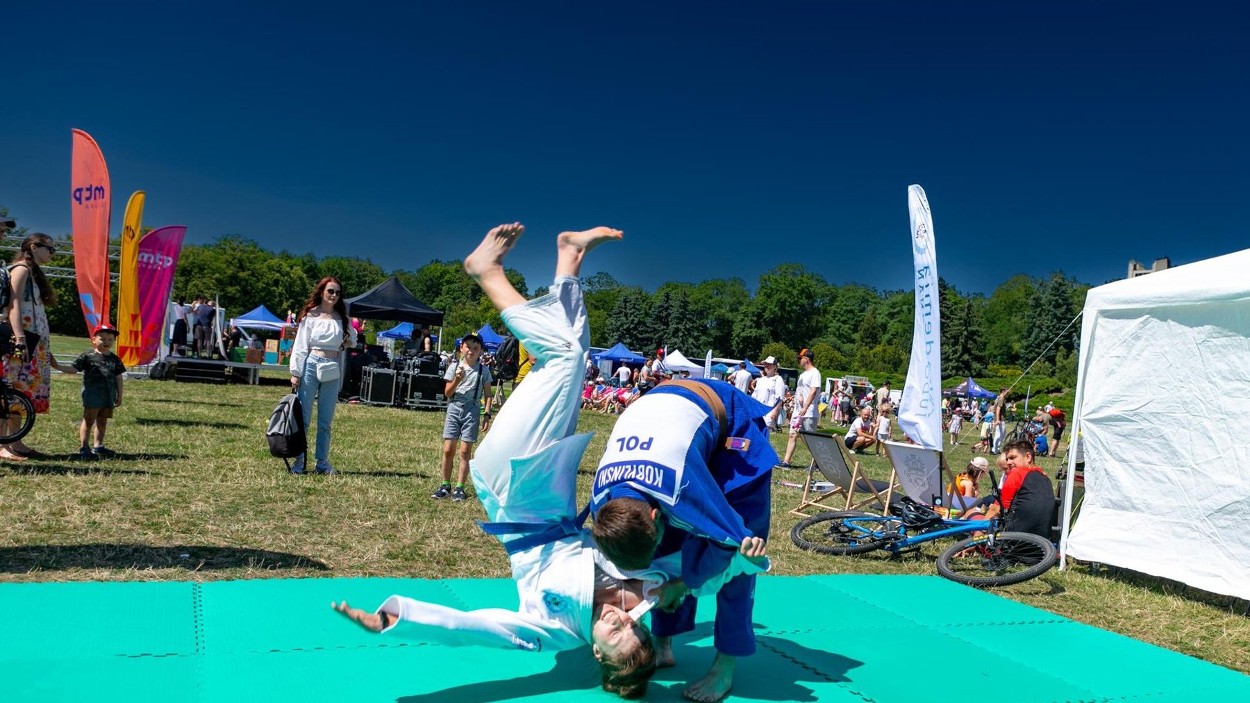 Na zdjęciu dwóch młodych judoków walczących na macie, w plenerze