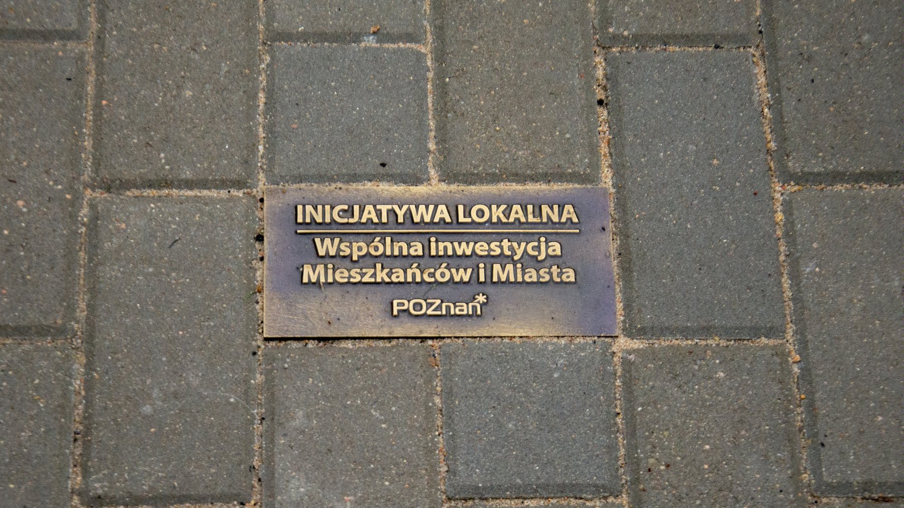 Pamiątkowa kostka chodnikowa z napisem "Inijcatywa lokalna. Wspólna inwestycja Mieszkańców i Miasta".