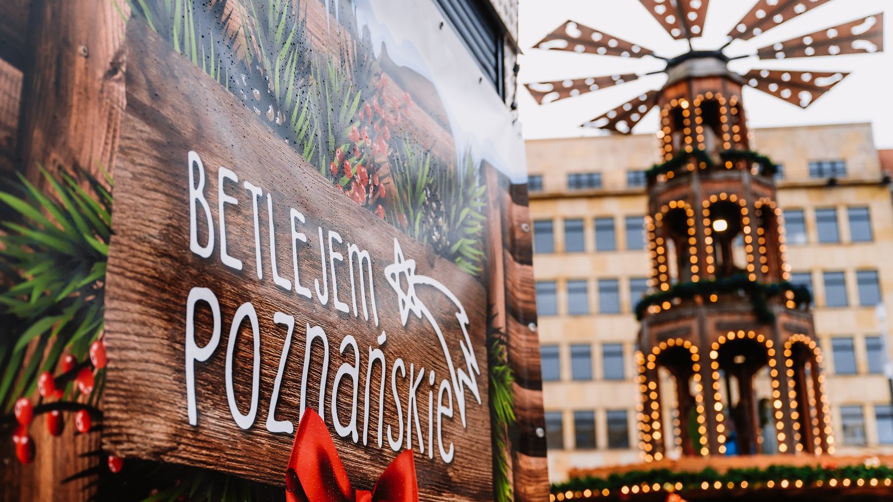 Zdjęcie przedstawia plakt z napisem Betlejem Poznańskie i udekorowaną światełkami instalacją.