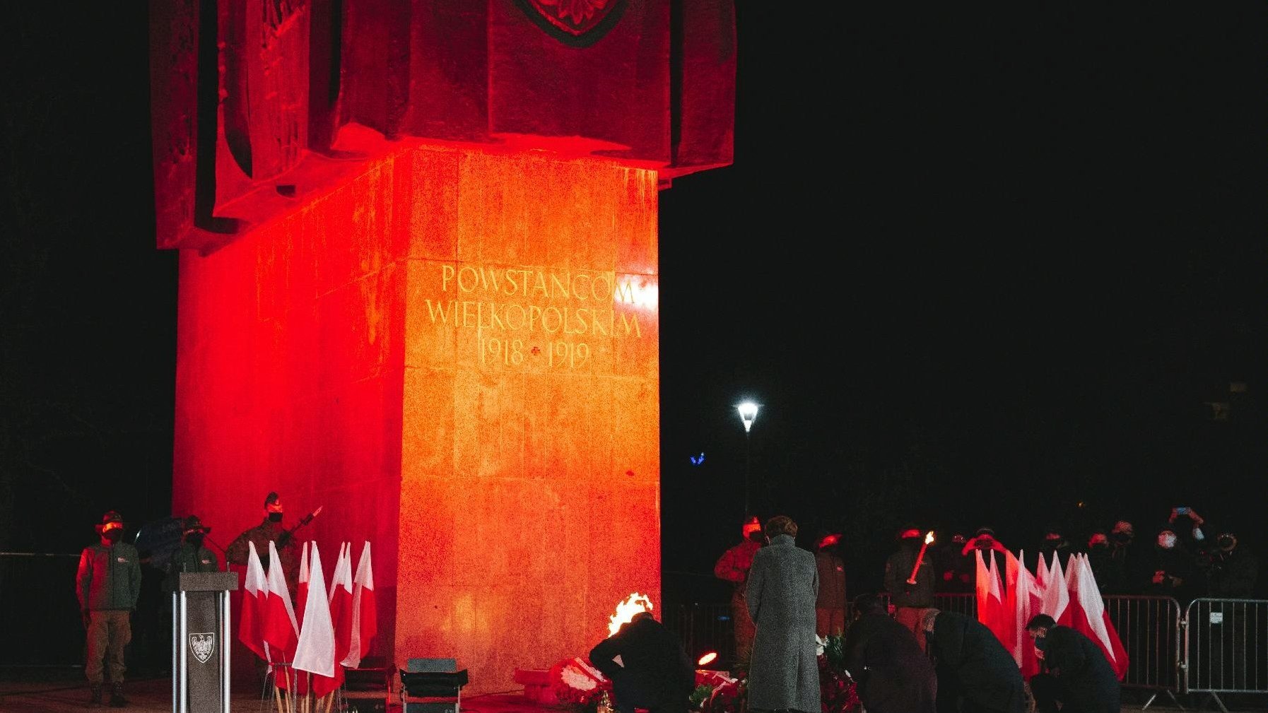 Zdjęcie przedstawia pomnik Powstańców Wielkopolskich i ludzi składającyh pod nim kwiaty.