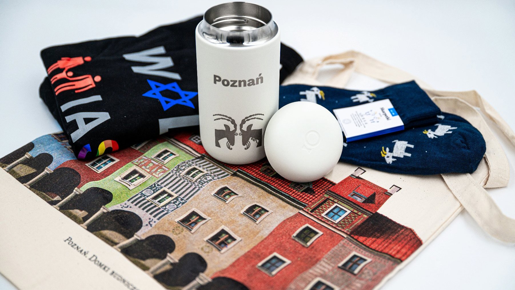 Zdjęcie przedstawia pakiet gadżetów promocyjnych, w skład których wchodzą m.in. koszulka "Wolne miasto Poznań", kubek termiczny z poznańskimi koziołkami i skarpetki.