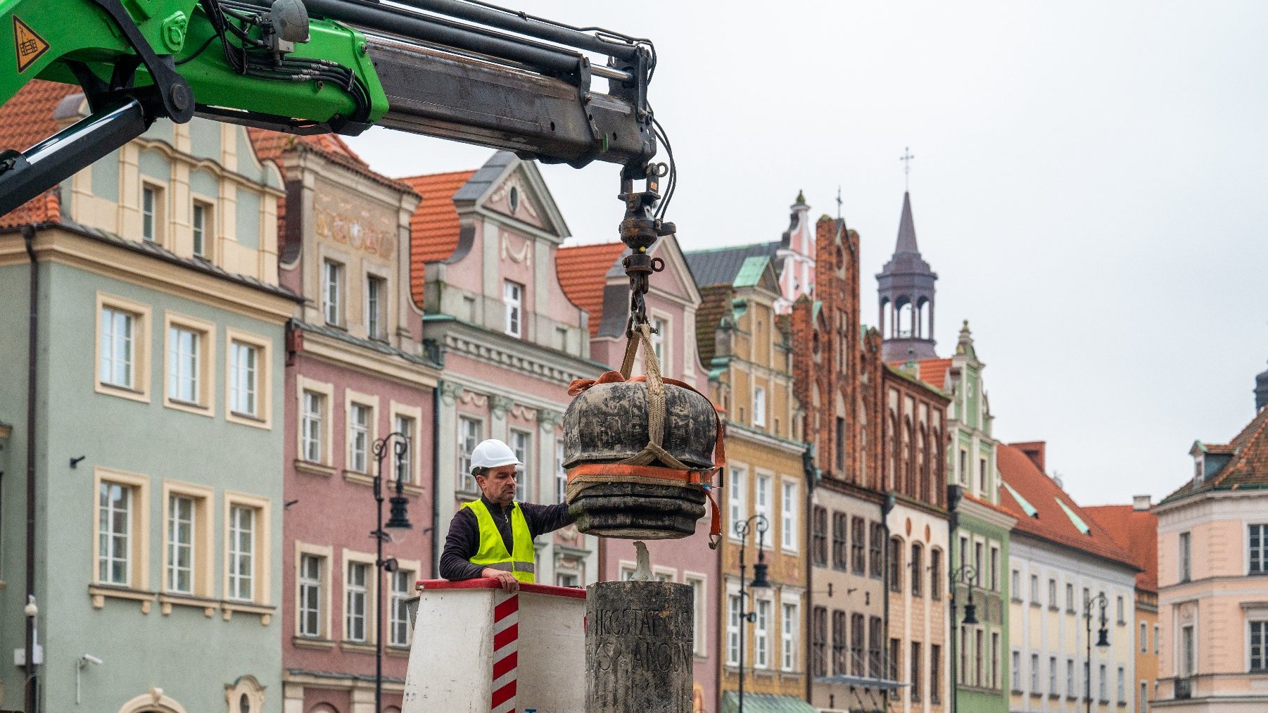 Na zdjeciu mężczyzna na podnośniku kontrolujący ustawienie pręgierza