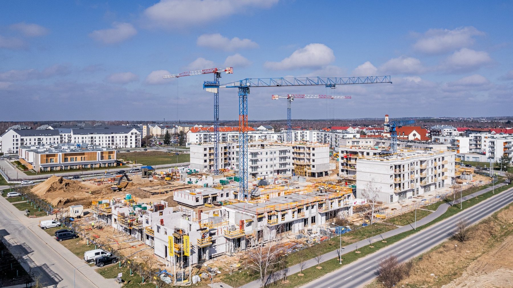 Zdjęcie z lotu ptaka przedstawia plac budowy, nad którym górują dzwigi.