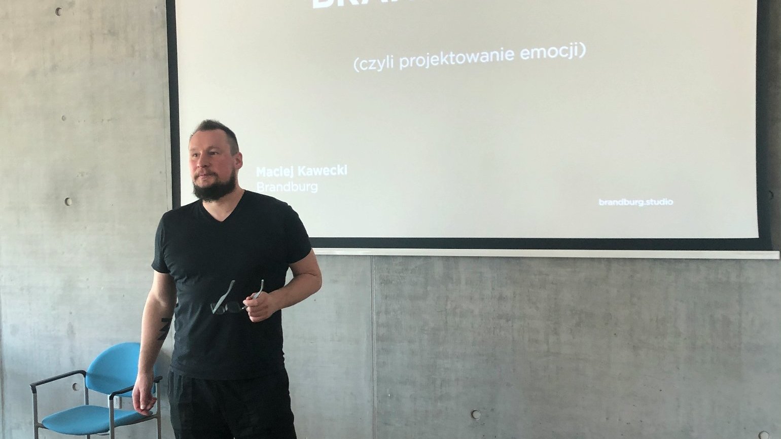 Na zdjęciu Maciej Kawecki, projektant, stojący przed ekranem, na nim prezentacja