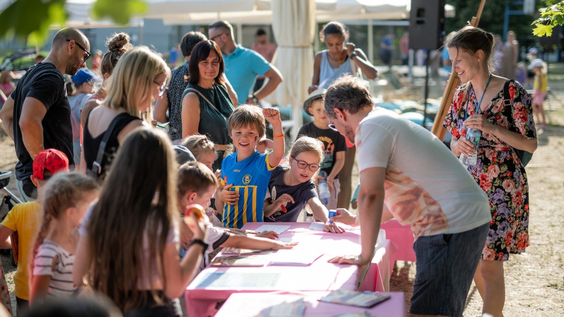 Zdjęcie przedstawia tłum dzieci i dorosłych przy stole podczas zajęć plastycznych.