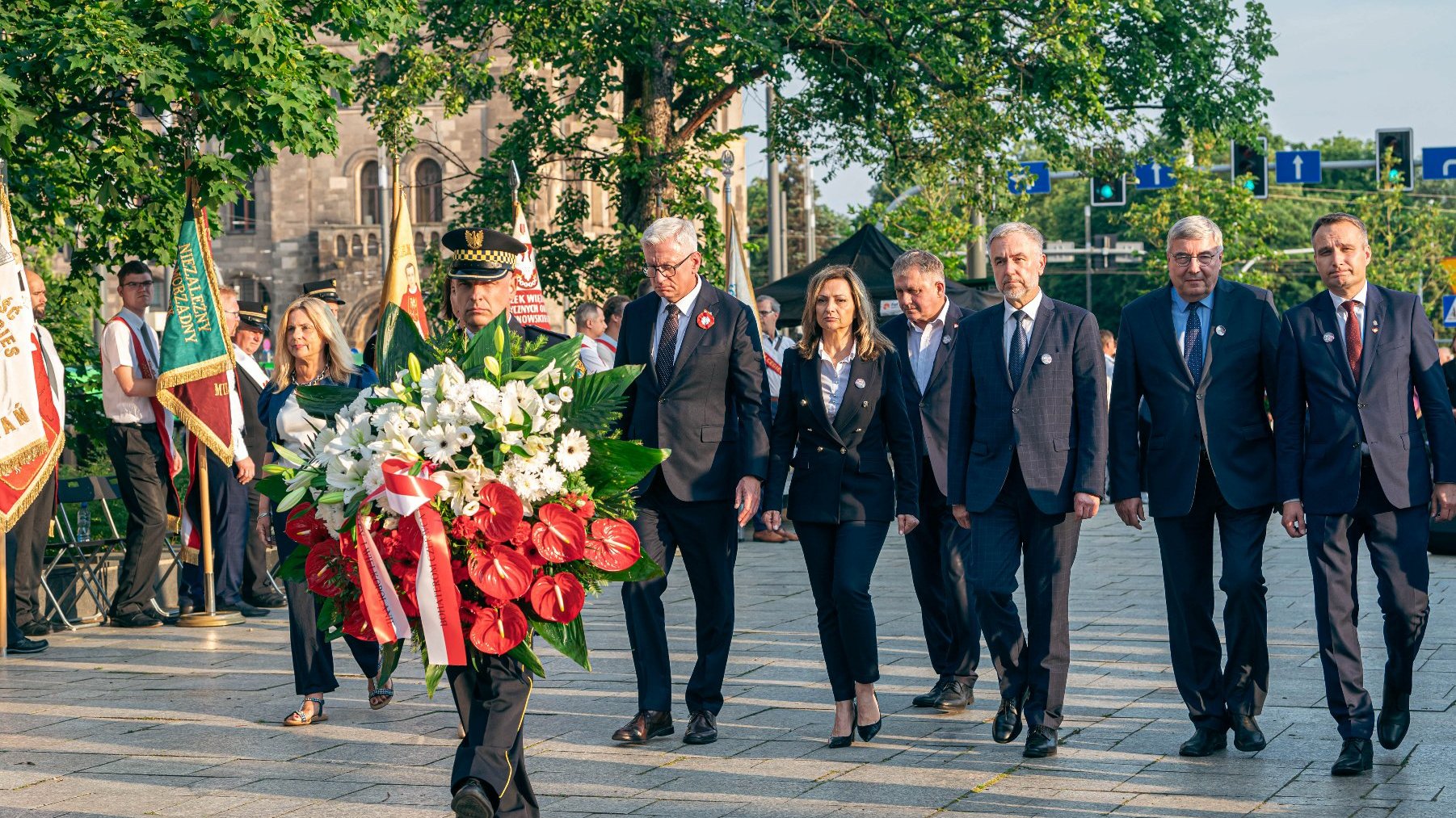 Na zdjęciu delegacja składająca kwiaty pod pomnikiem,na pierwszym planie strażnik miejski z wiązanką