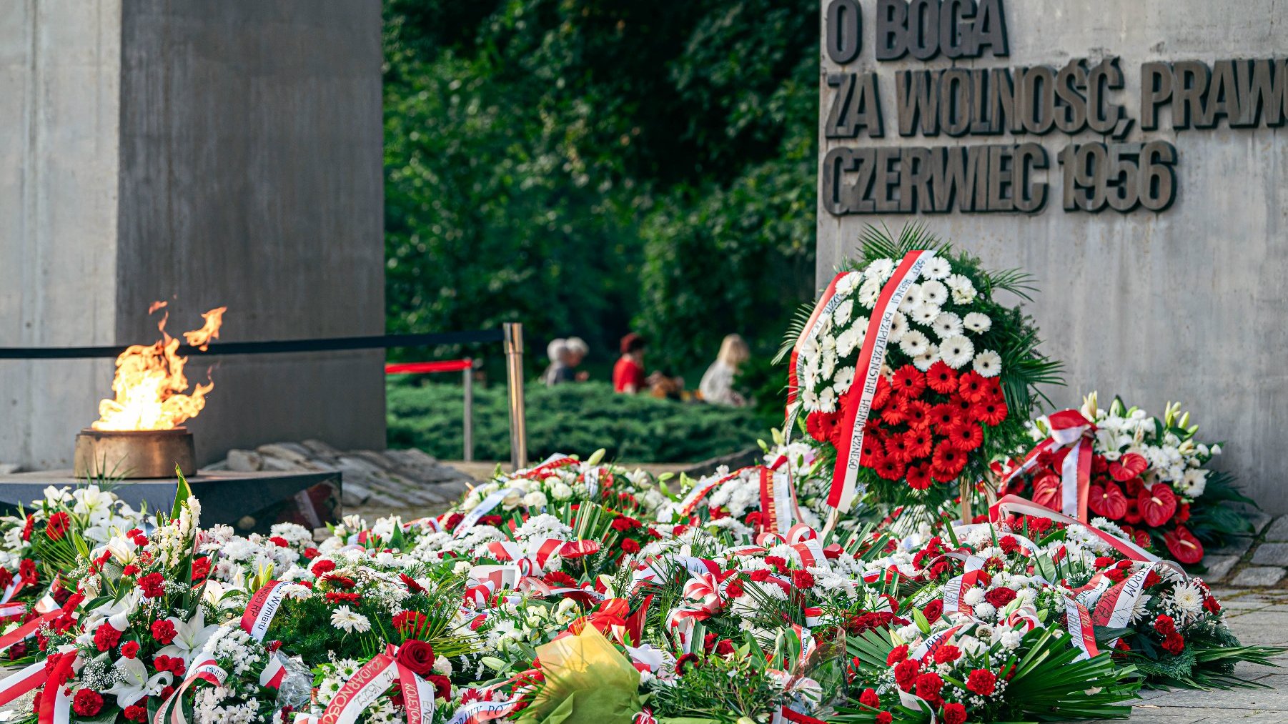 Na zdjęciu pomnik, pod nim kwiaty i płonący znicz