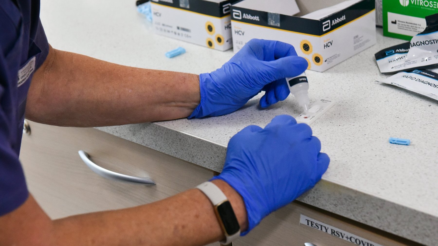 Na zdjęciu dłonie w medycznych rękawiczkach zakraplają test kasetkowy