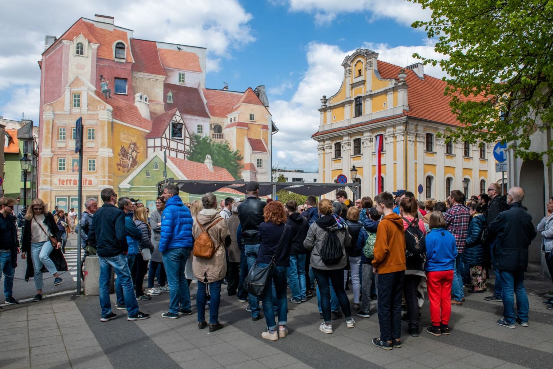 Grupa ludzi stoi przy muralu na Śródce podczas oprowadzania z przewodnikiem. - grafika artykułu