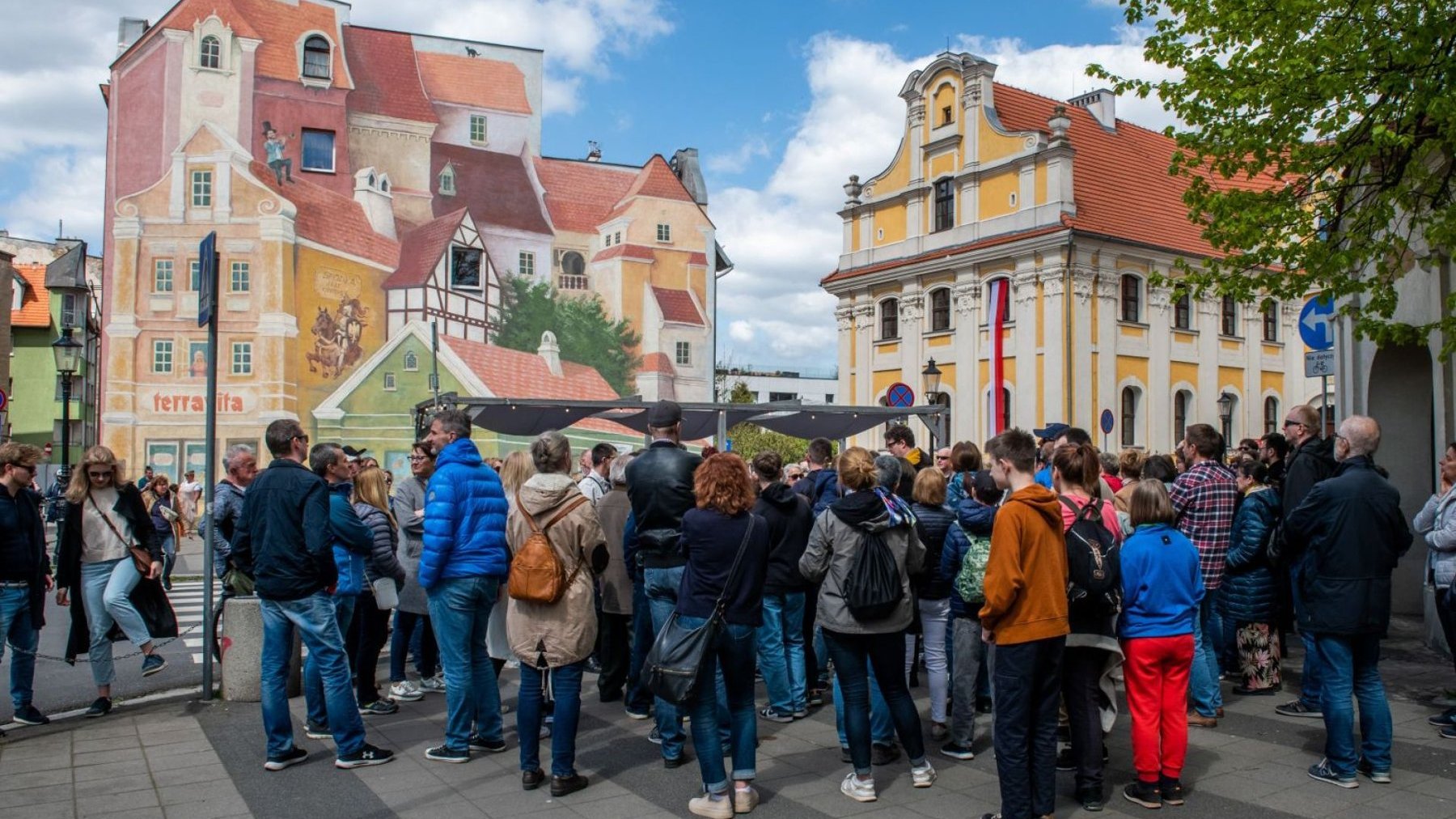 Grupa ludzi stoi przy muralu na Śródce podczas oprowadzania z przewodnikiem.