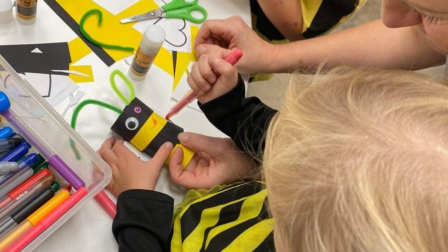 Zdjęcie przedstawia dzieci tworzące pszczołę z papieru. Na zdjęciu widać tylko ich ręce i materiały plastyczne.
