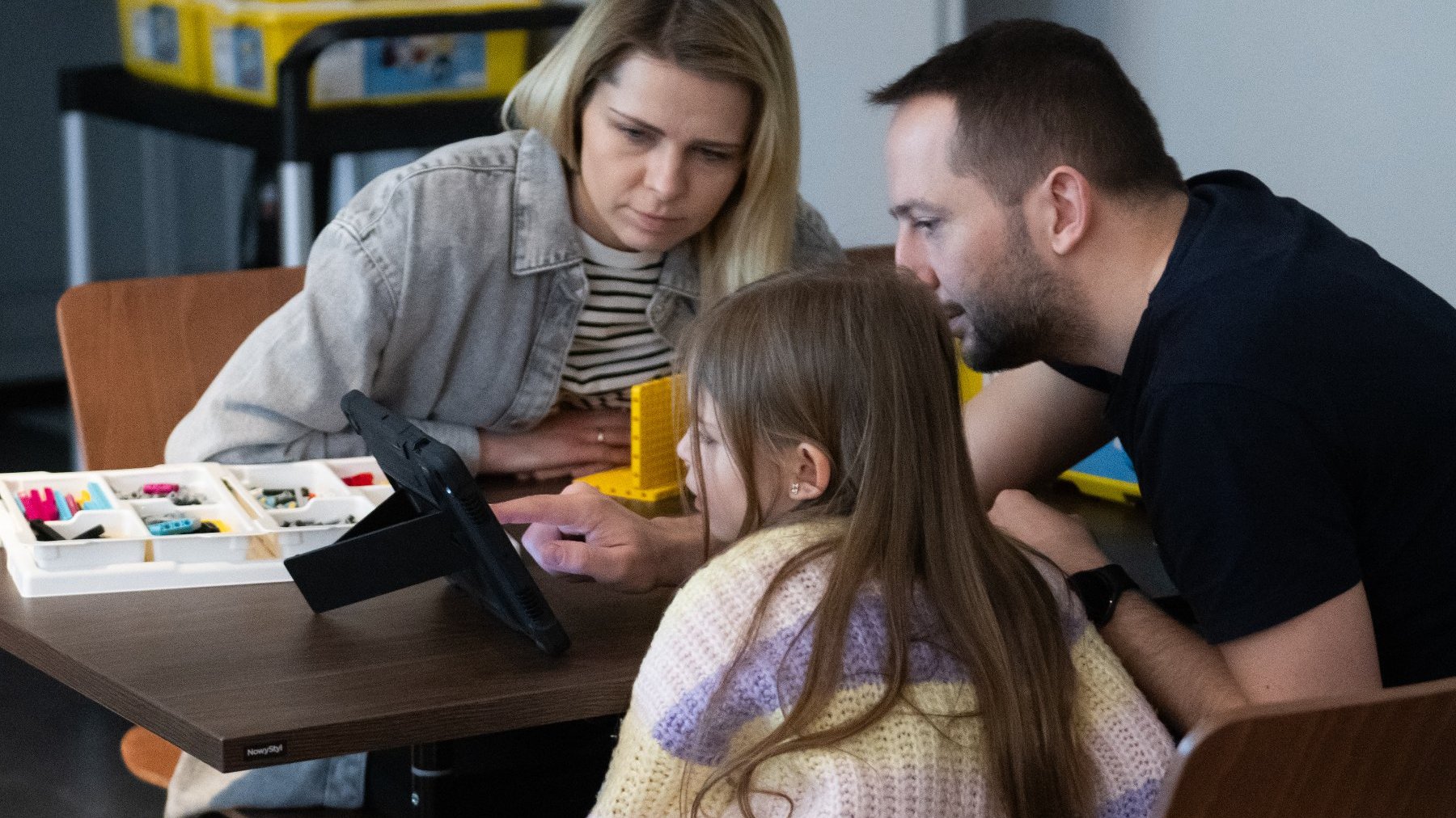 Zdjęcie przedstawia kobietę, mężczyznę i dziewczynkę siedzących przy stole podczas zajęć.