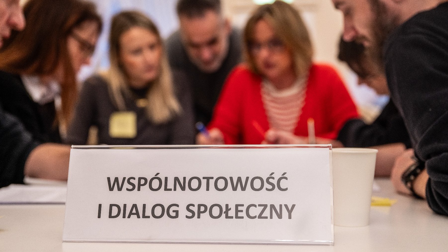 Na zdjęciu kilka dyskutujących osób, na pierwszym planie tabliczka z napisem: wspólnotowość i dialog społeczny