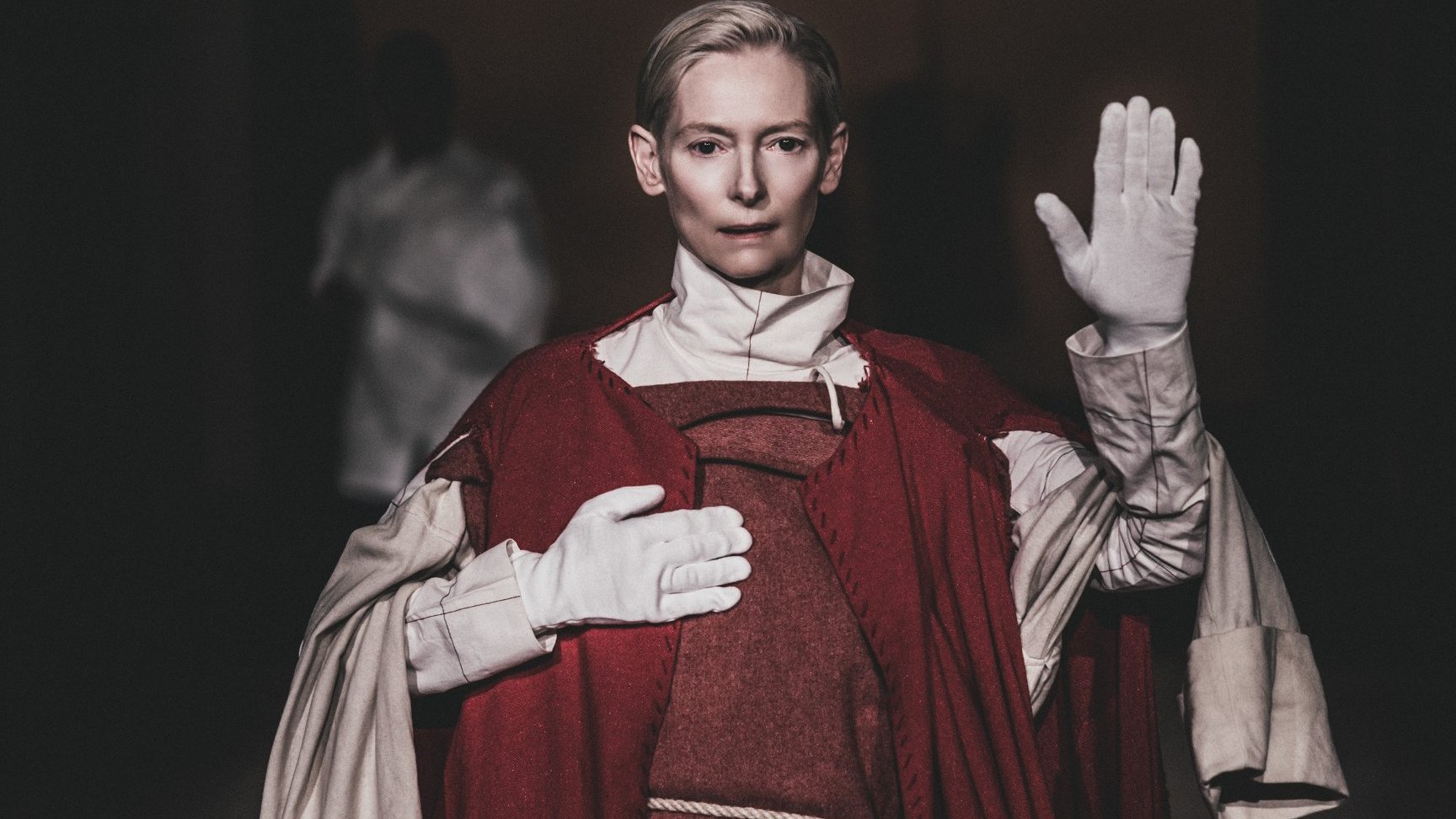 Na zdjęciu Tilda Swinton z jedną dłonią uniesioną w górze