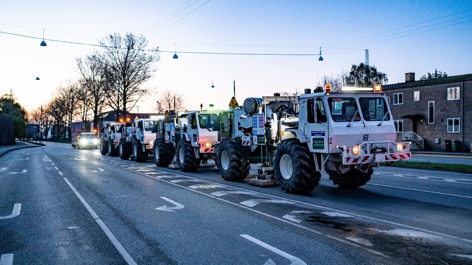 Zdjęcie przedstawia ciężarówki do pomiarów sejsmicznych jadące ulicą o zmierzchu.