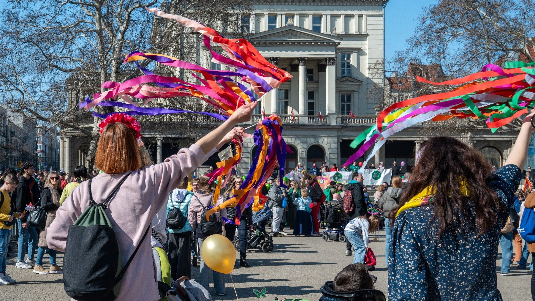 Na zdjęciu tłum zebrany na placu Wolności, na pierwszym planie dwie kobiety machające kolorowymi wstęgami